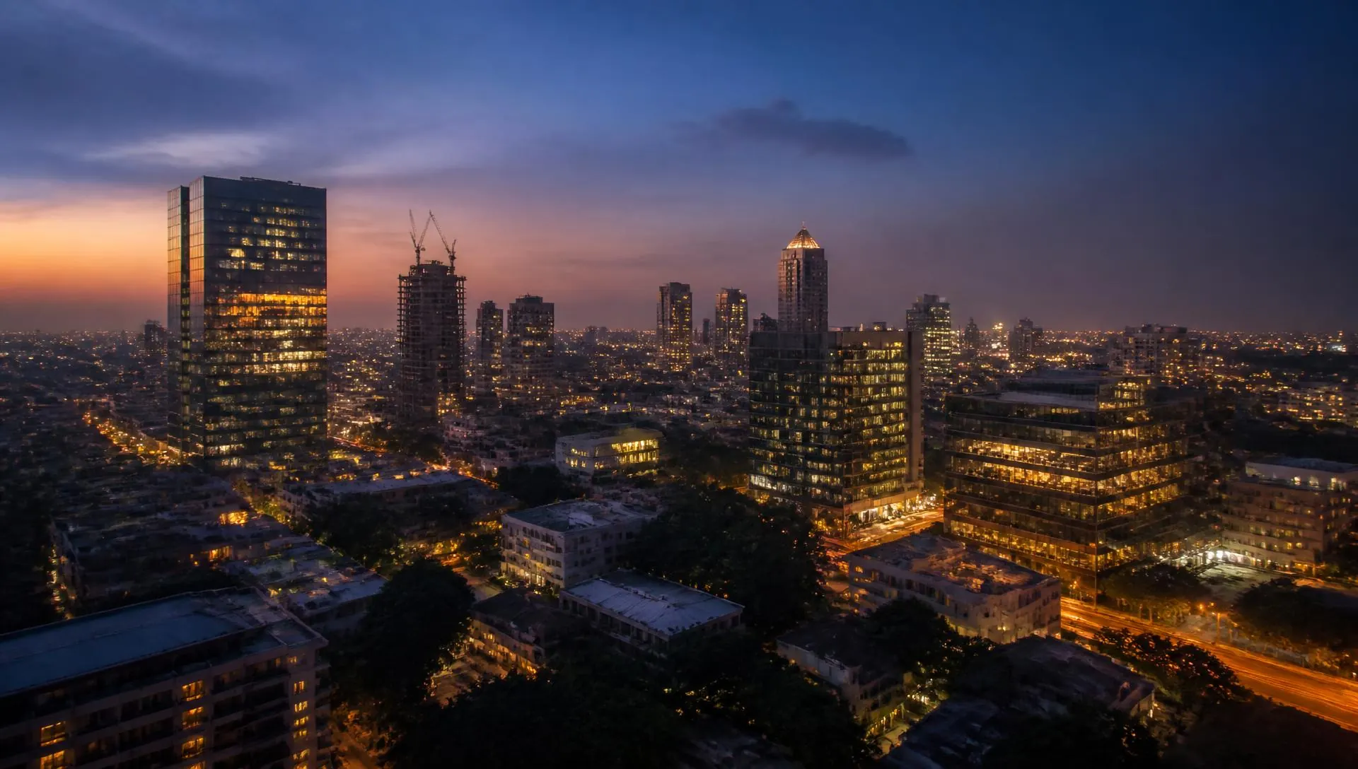 Bengaluru skyline at dusk, glass towers and construction cranes lit by city lights